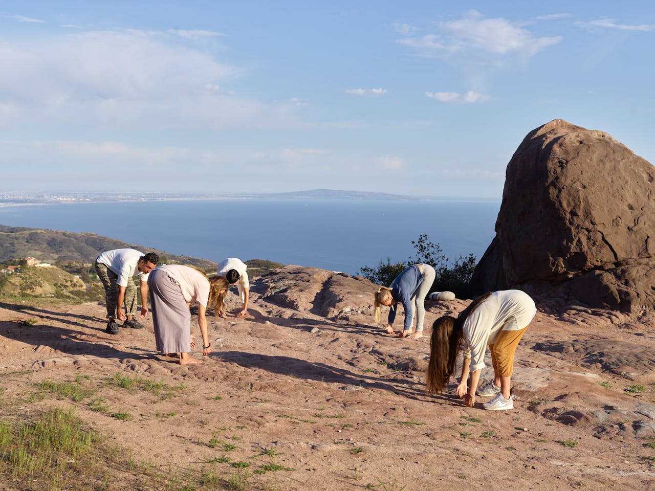 Group of adults practicing yoga stretches on a cliff with ocean views, promoting relaxation and mindfulness.